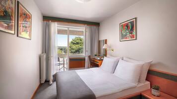 Habitación de hotel con cama, escritorio, silla, ventana con cortinas y obras de arte en las paredes.