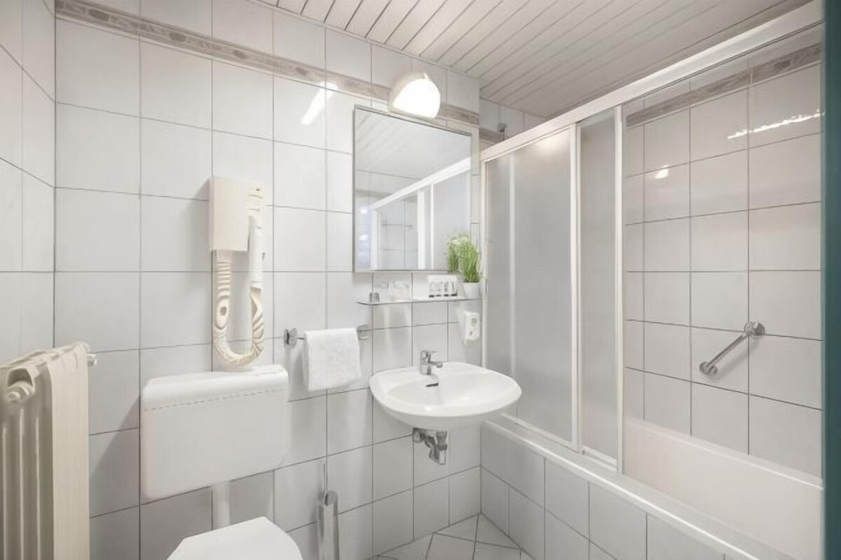 A bathroom with a toilet, sink, mirror, and shower.