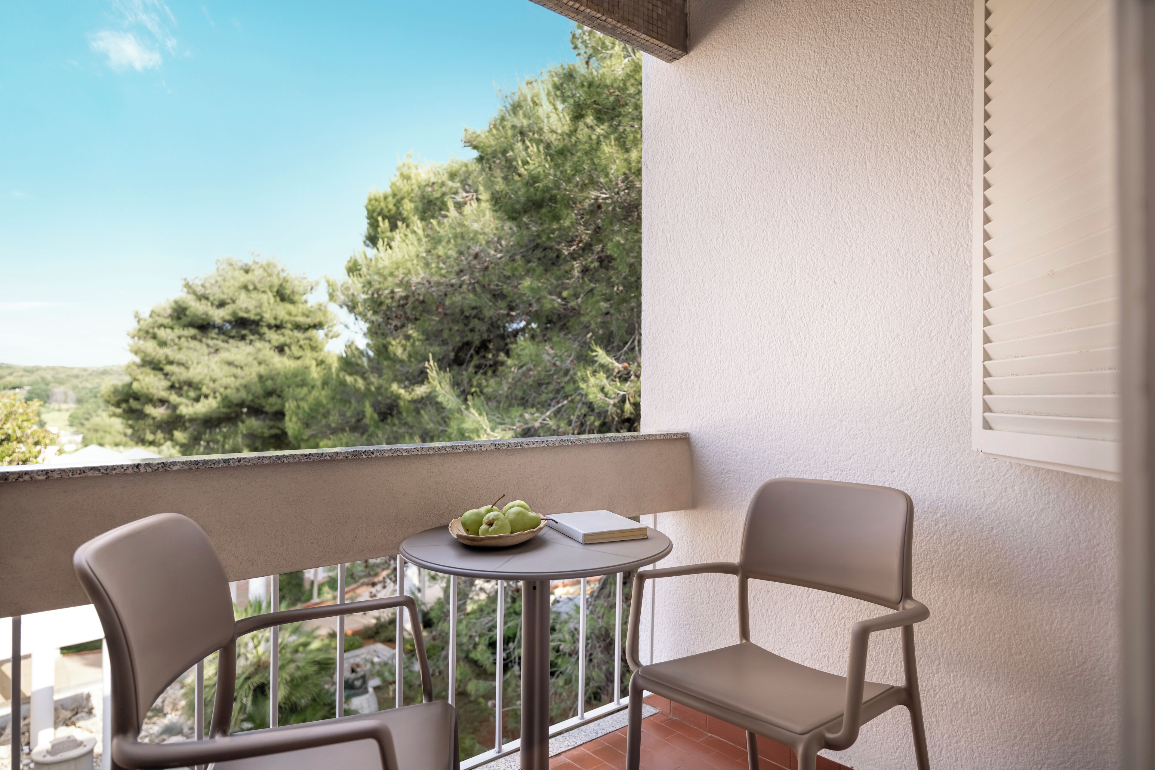 Een balkon met twee stoelen, een klein tafeltje en een schaal groene appels.