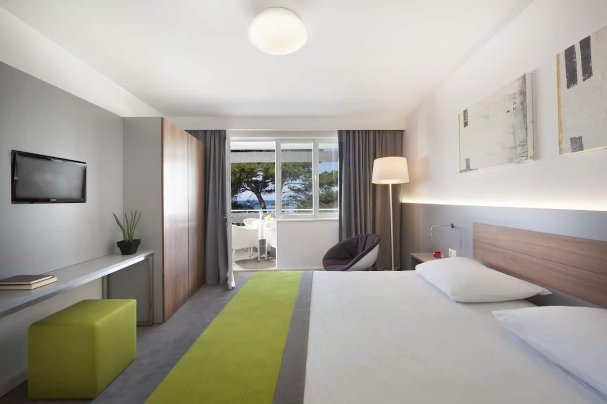 Quarto de hotel moderno com cama, escrivaninha, cadeira, televisão e vista para o exterior.