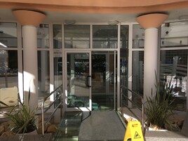 Entrada de hotel con puertas de vidrio, una rampa y plantas en macetas.