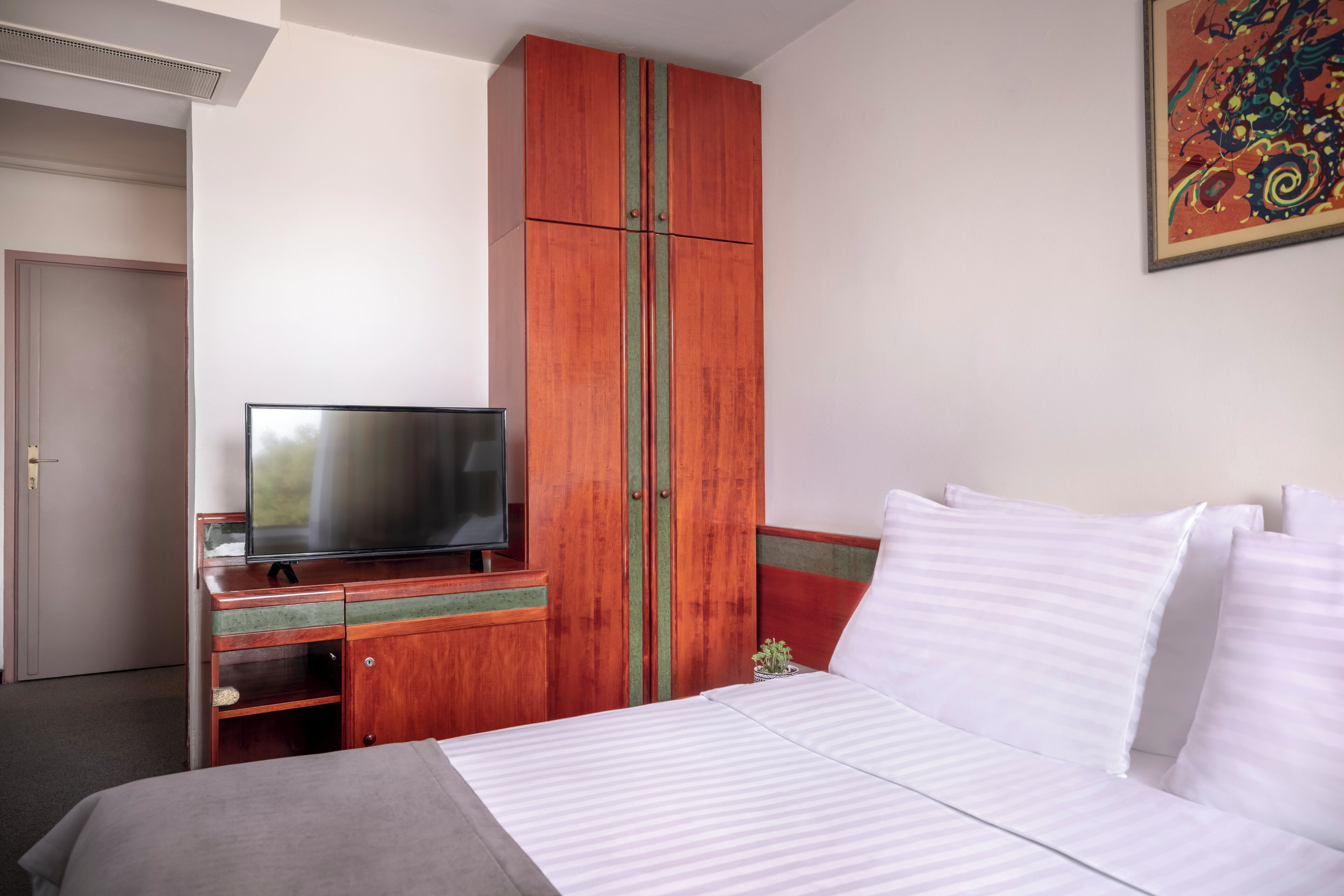 A hotel room with a bed, a television on a wooden cabinet, and a painting on the wall.
