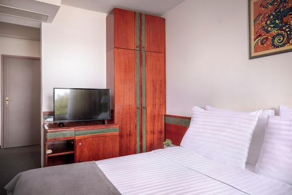 Une chambre d’hôtel avec un lit, un téléviseur posé sur une commode en bois et un tableau accroché au mur.