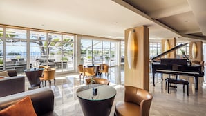 Un amplio salón con un piano de cola, asientos cómodos y grandes ventanales que ofrecen vistas al exterior.