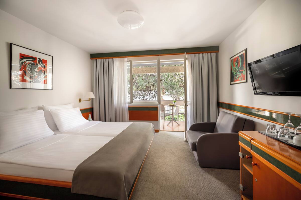 Quarto de hotel com duas camas, televisão, escrivaninha e uma cadeira.