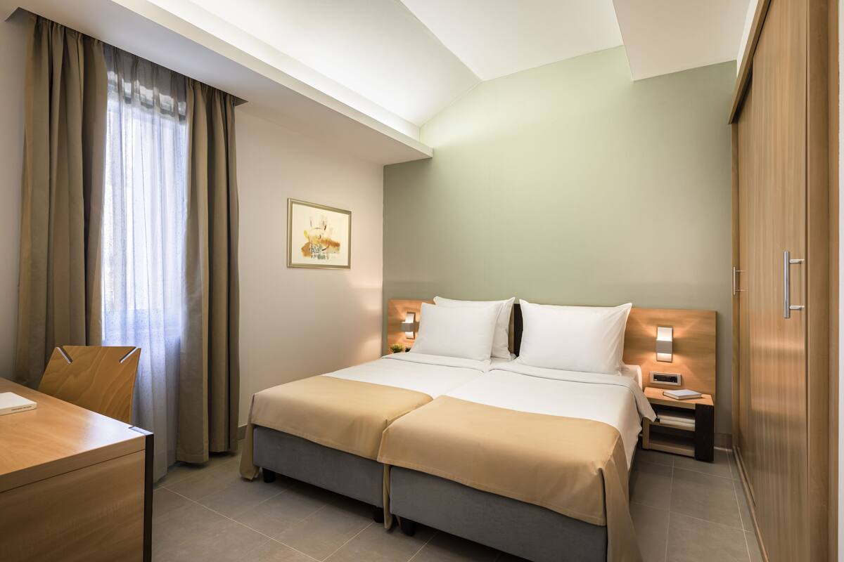 A hotel room with a bed, bedside tables, a desk, and a chair.