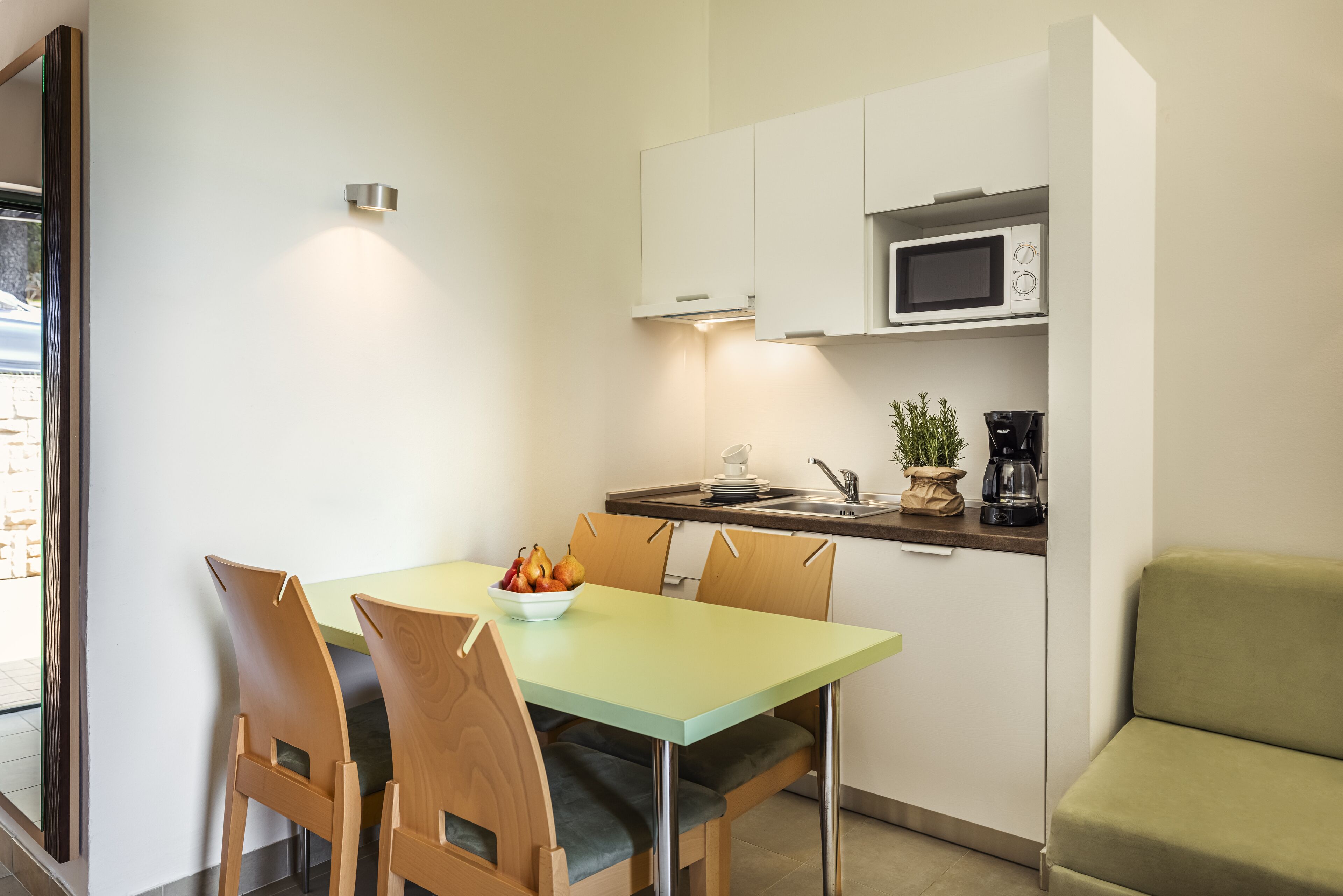 A compact kitchen with a microwave, coffee maker, and a bowl of fruit on the counter.