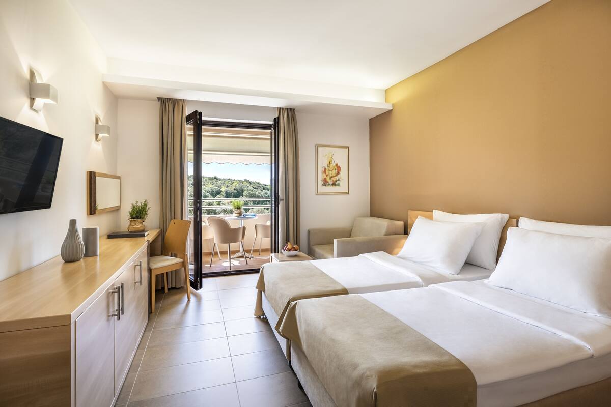 A hotel room with two beds, a desk with a chair, a TV, and a balcony with a view.