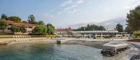 A waterfront hotel with a pool, lounge chairs, and umbrellas.