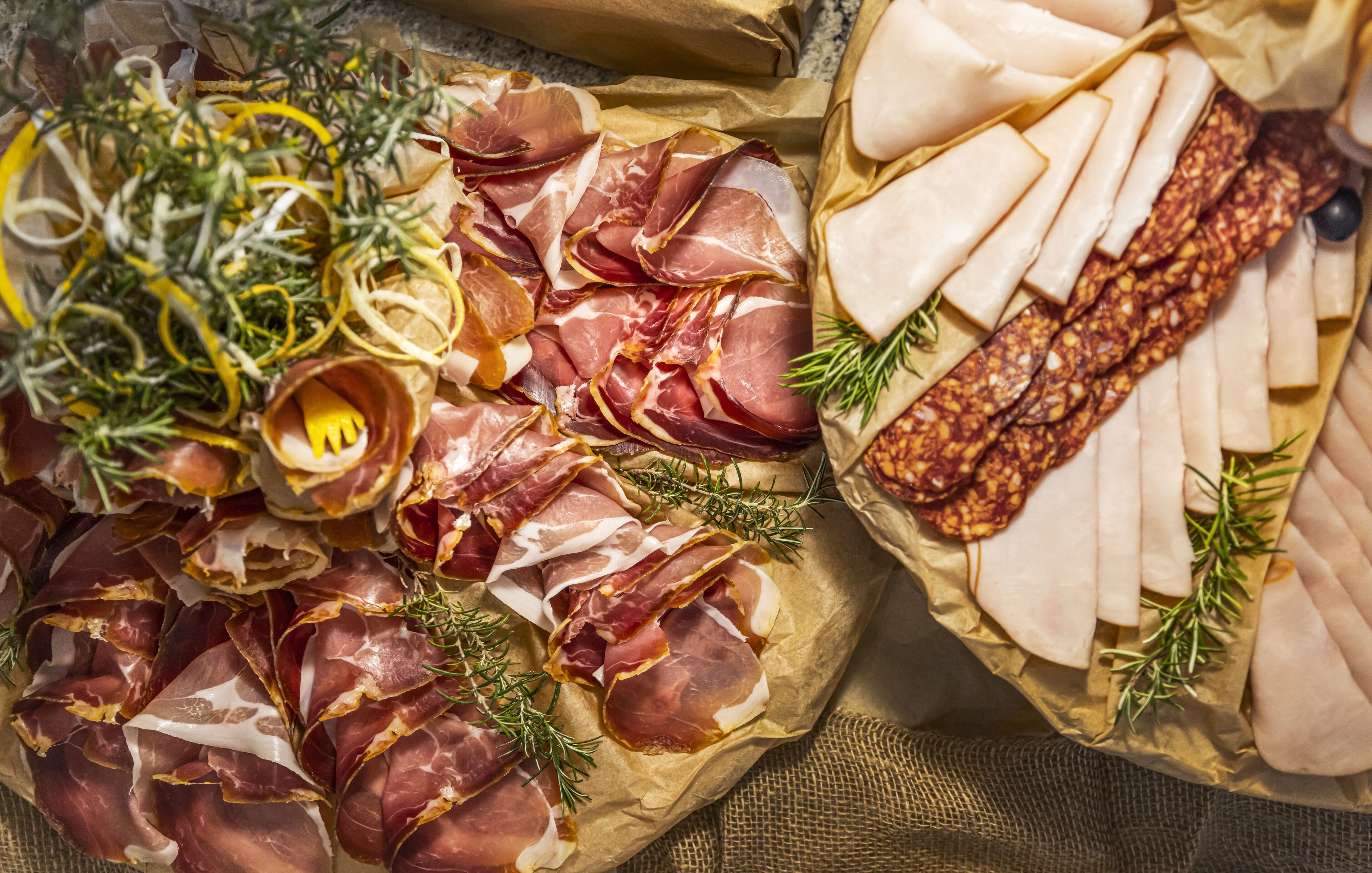 A variety of cured meats and cheeses arranged on parchment paper, garnished with herbs.