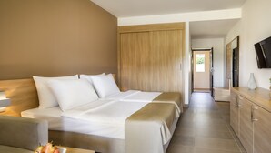 Habitación de hotel con una cama grande, una mesita de noche con fruta, un armario de madera, un televisor y un baño visible a través de una puerta abierta.
