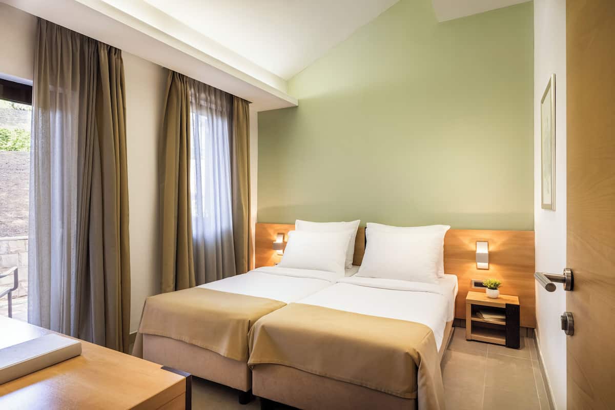 A hotel room with a bed, bedside tables, a desk, and curtains.