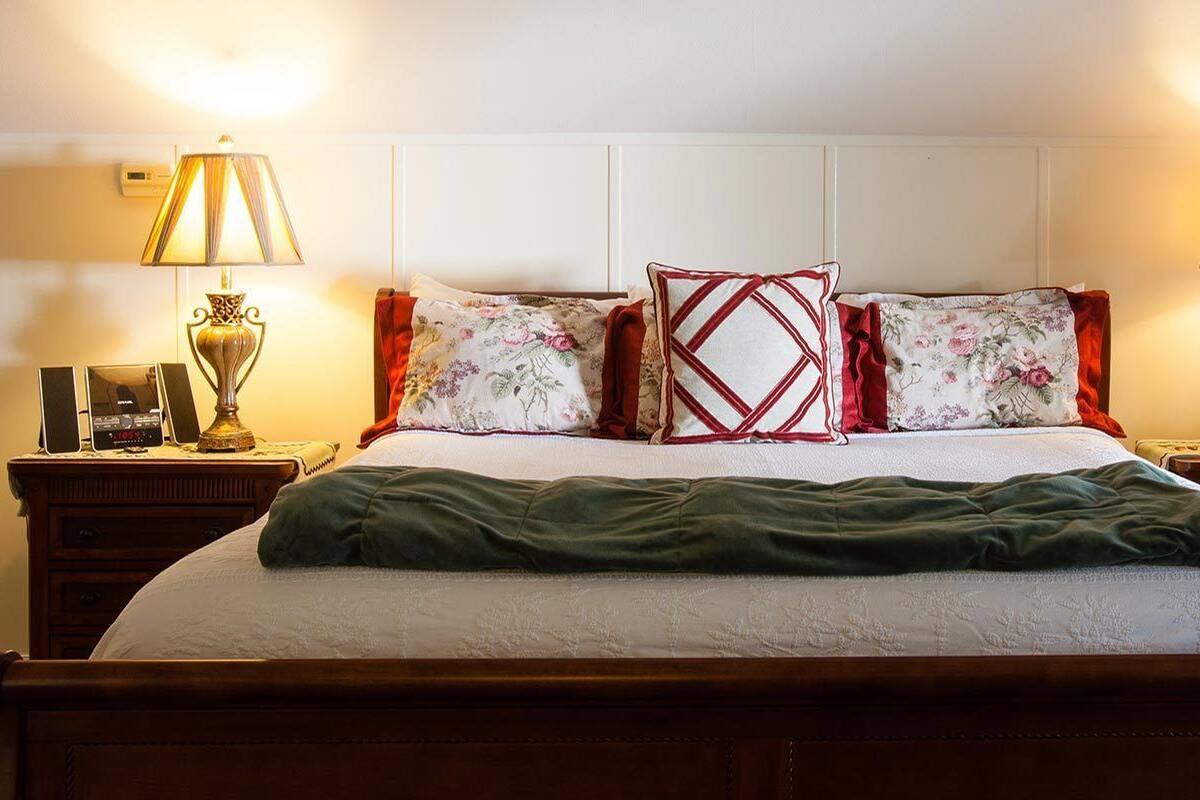 Ein ordentlich bezogenes Bett mit grüner Decke, zwei Nachttische mit Lampen und blumenmusterbesetzte Kissen.