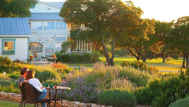 A couple sitting at a table in a garden with a house in the background.