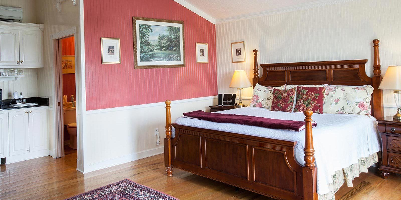 Ein Schlafzimmer mit einem hölzernen Himmelbett, einer roten Akzentwand und einem großen gerahmten Bild.