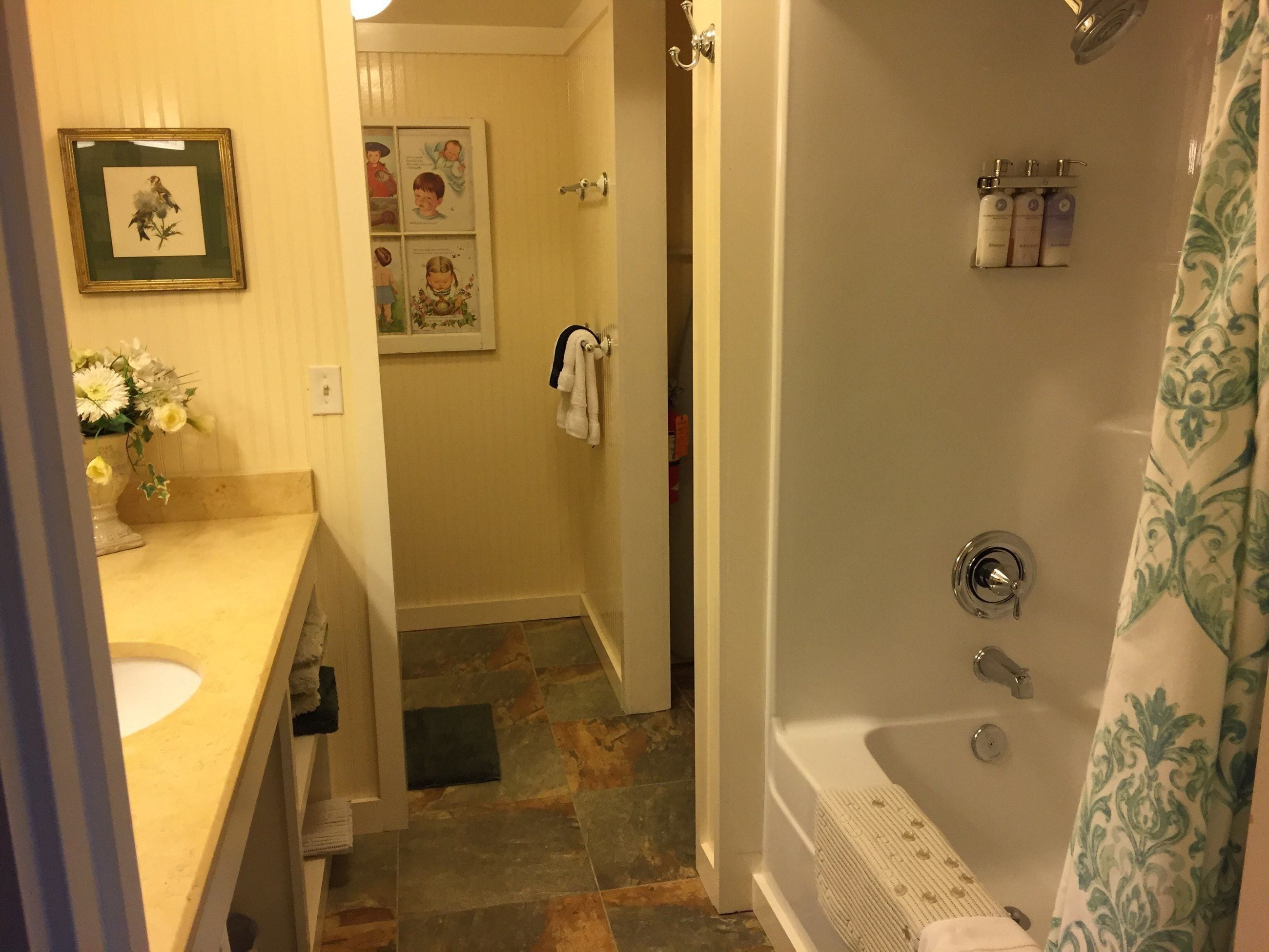 A bathroom with a bathtub, a sink, and a shower. There are framed pictures on the wall and a towel rack.