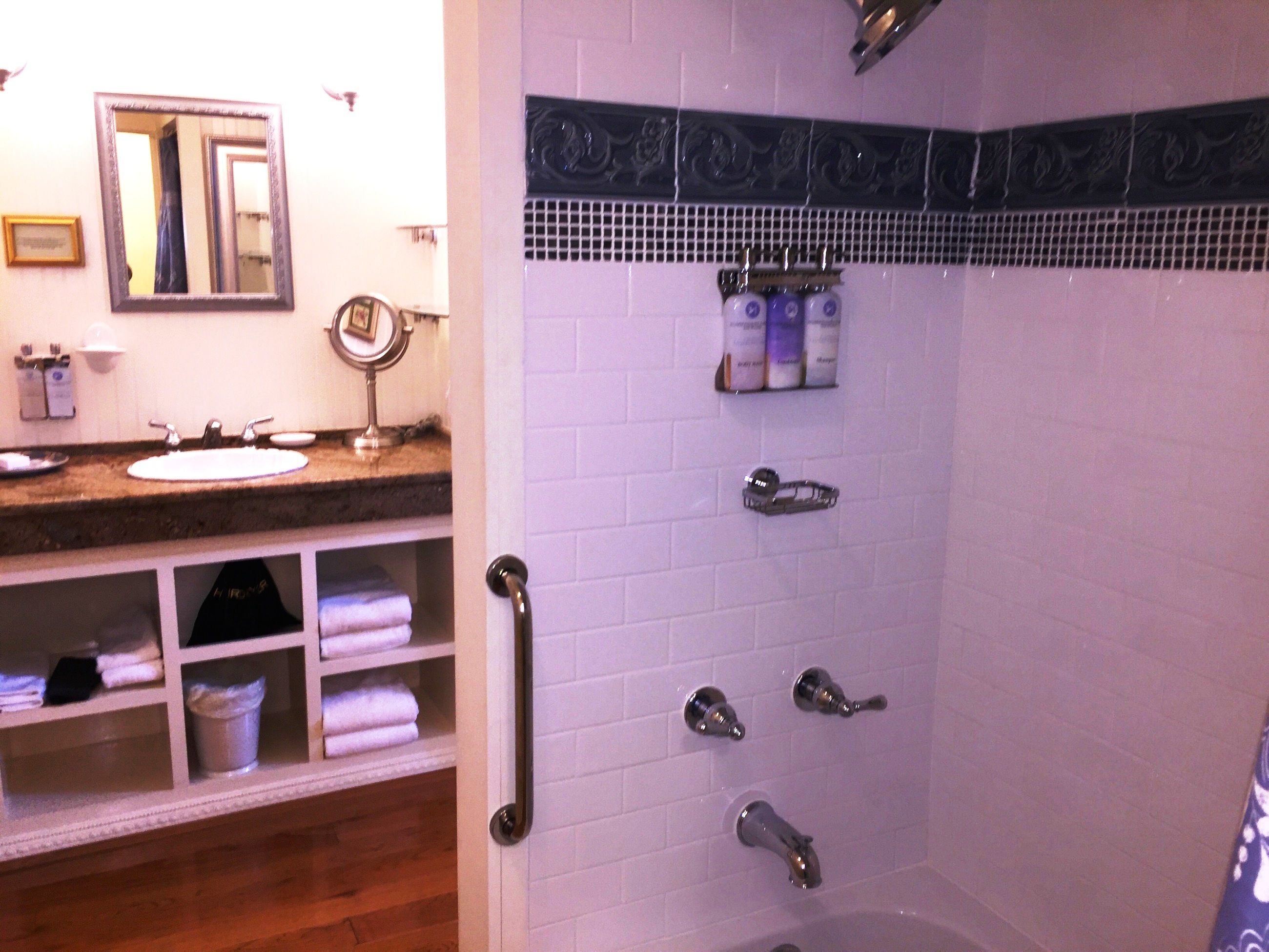 A bathroom with a sink, mirror, towel rack, and a shower with multiple faucets.