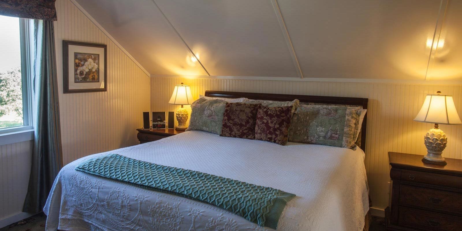 Un lit bien fait, agrémenté d’un plaid vert, deux lampes de chevet et un tableau encadré au mur.