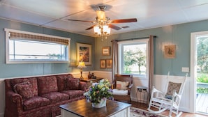 A living room with a sofa, a coffee table with a floral centerpiece, a rocking chair, and a ceiling fan.