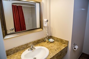 A bathroom with a granite countertop sink, a mirror, a hairdryer, and a toilet paper holder.
