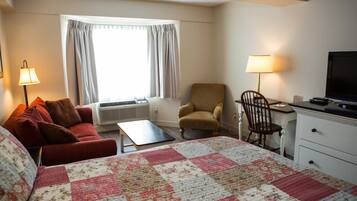 A hotel room with a large bed, a red sofa, a small table, a desk with a chair, a TV, and a window with curtains.