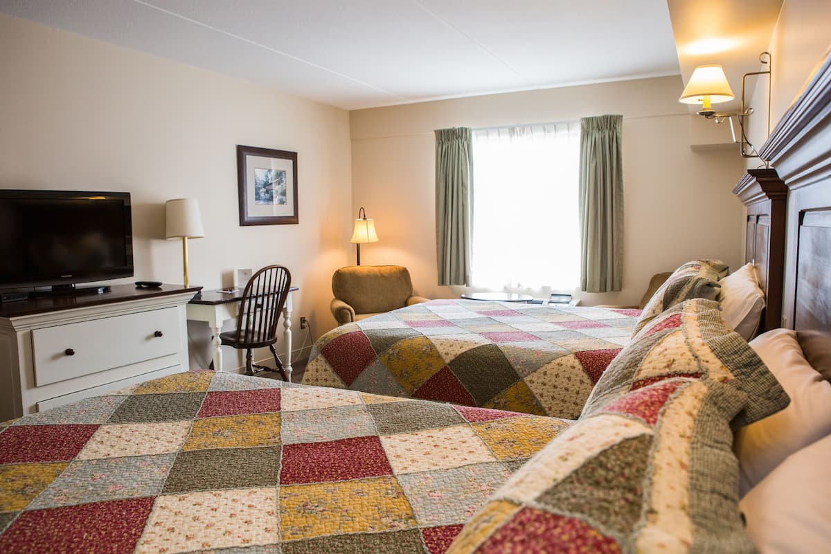 A hotel room with two beds, a desk with a television, a chair, a lamp, and a window with curtains.