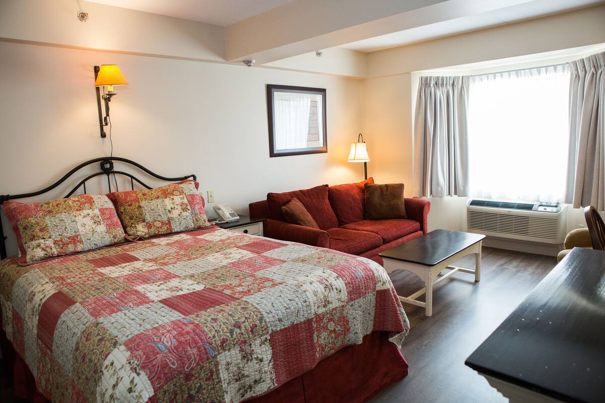 A hotel room with a large bed, a red sofa, a small table, and a window with curtains.