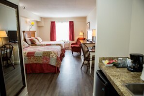 A hotel room with two beds, a desk with a computer, a chair, a television, and a kitchenette with a coffee maker.