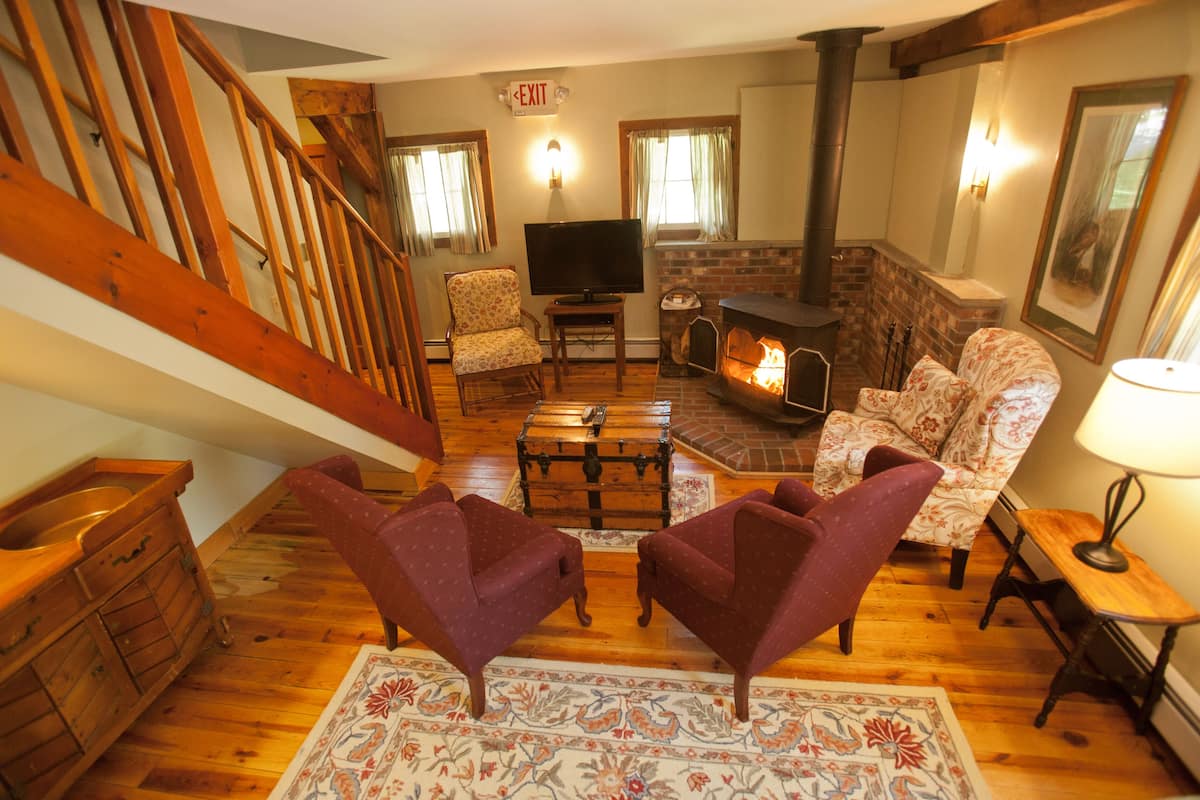 A cozy living room with a fireplace, wooden flooring, a television, and two armchairs.