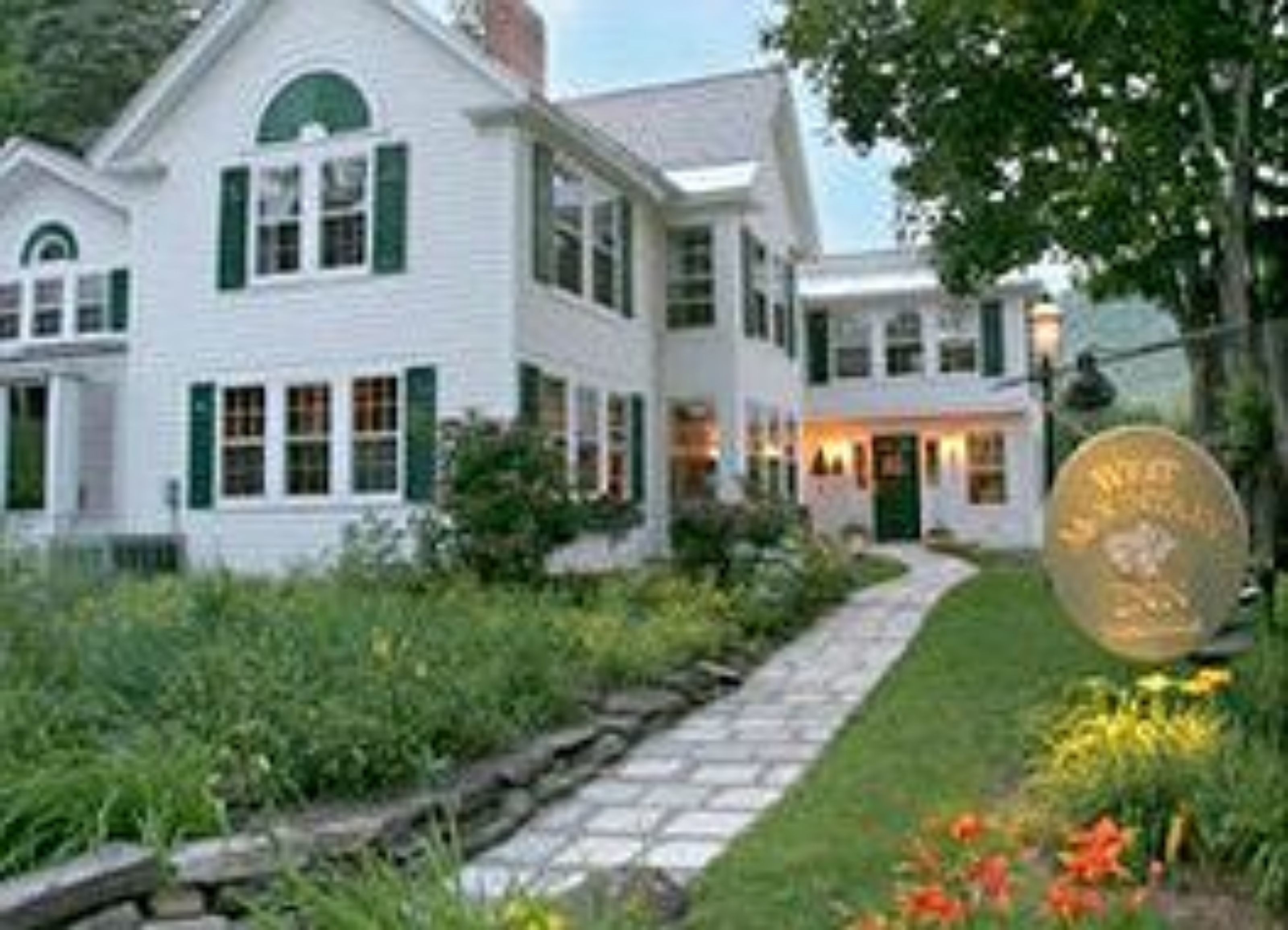 A two-story white house with green shutters and a stone pathway leading to the entrance.