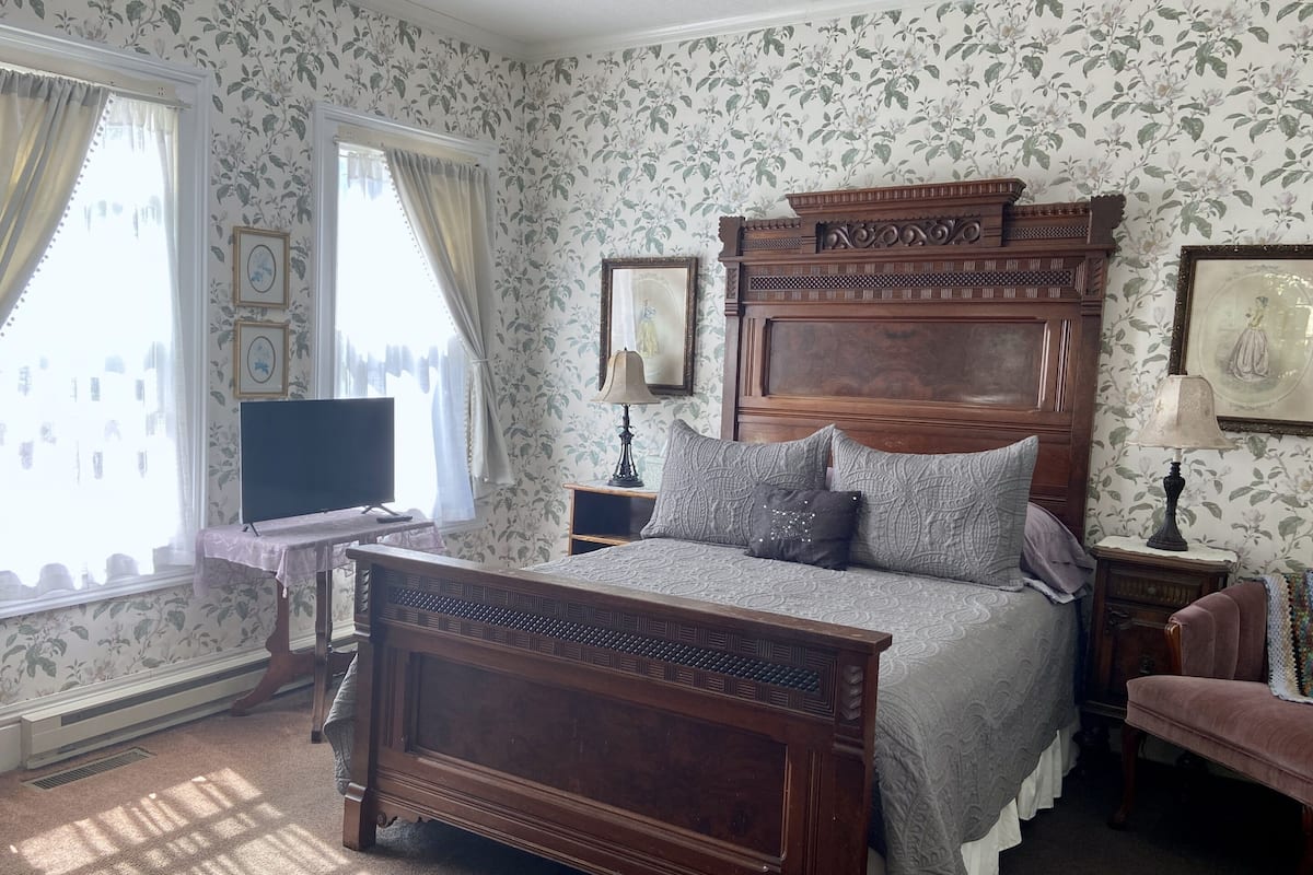 A traditional bedroom with a four-poster bed, a television, and floral wallpaper.