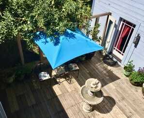 A wooden deck with a blue umbrella, a metal table, chairs, and a stone fountain. - Shaw House Inn (Ferndale)