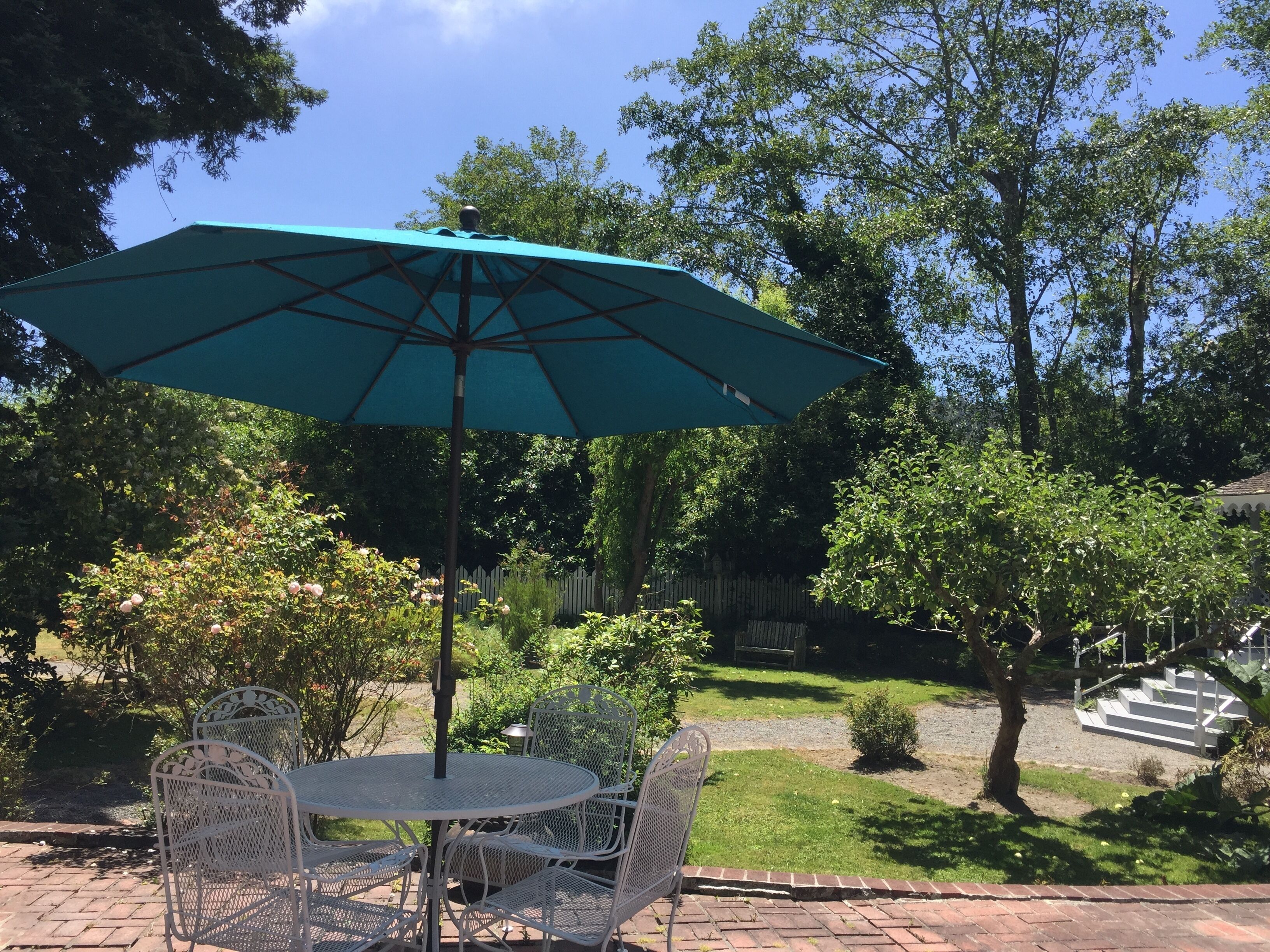 A patio with a round table and chairs, a green umbrella, and a brick pathway.