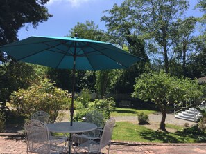 A patio with a round table and chairs, a green umbrella, and a brick pathway. - Shaw House Inn (Ferndale)