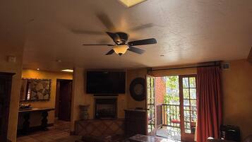 A living room with a ceiling fan, a fireplace, a television, and a view of the outdoors through a window.