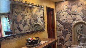 Un muro in pietra con una statua, una panca di legno con un cesto e uno specchio con cornice decorativa.