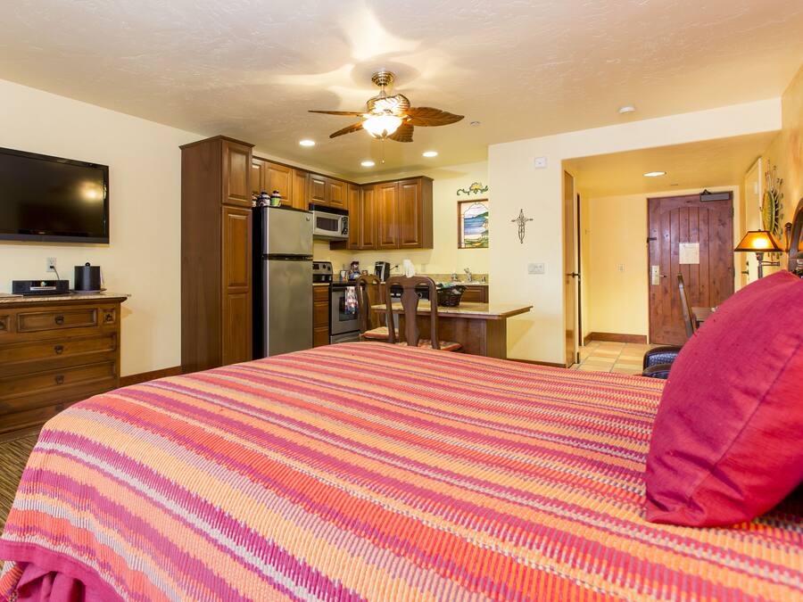 A bedroom with a large bed, wooden cabinets, a flat-screen TV, and a ceiling fan.
