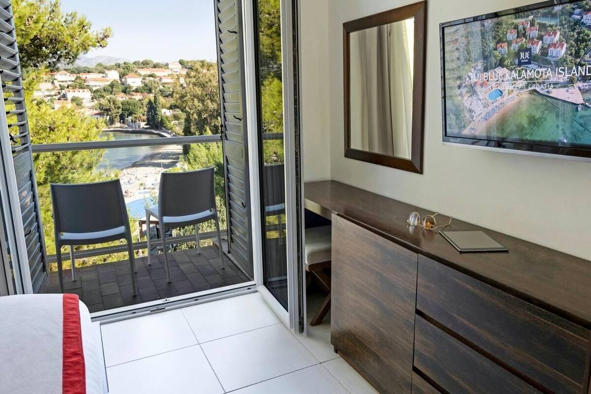 Une chambre avec un balcon, une télévision, une armoire en bois et un lit.