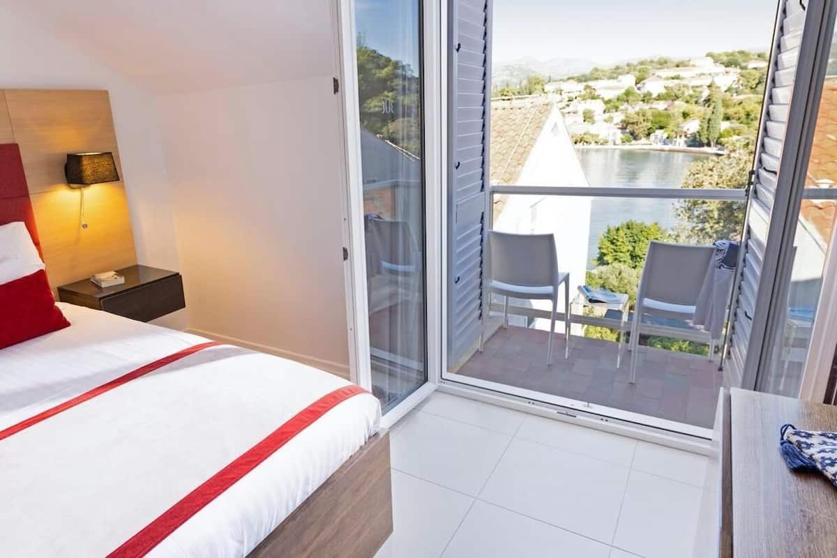 Une chambre d’hôtel avec un lit, une table de chevet, une lampe, un balcon avec des chaises et une vue sur le paysage.