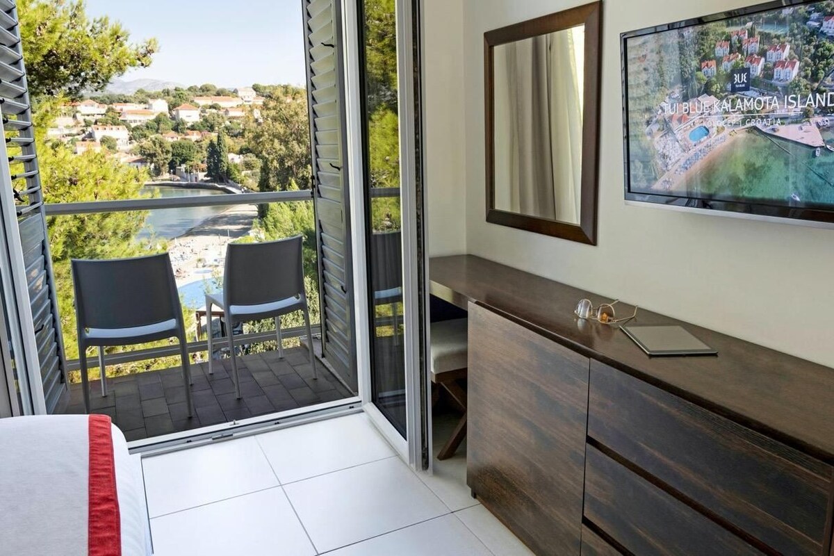 A room with a balcony, a TV, a wooden cabinet, and a bed.
