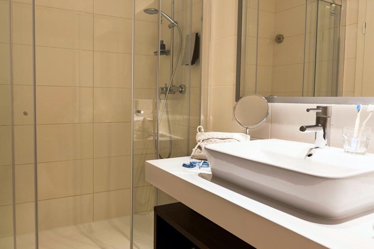 A modern bathroom with a glass shower enclosure, a white sink with a mirror, and a towel rack.