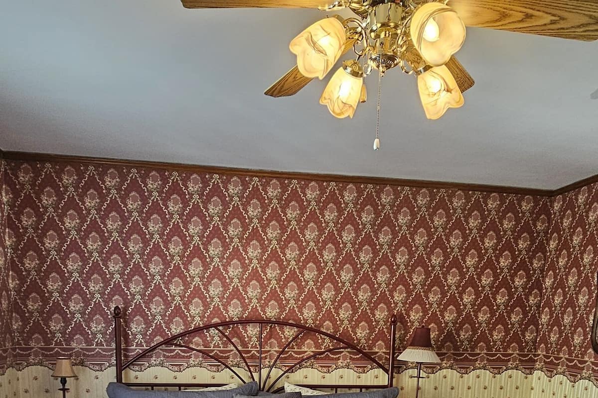 A bedroom with a bed, a wooden bench, a ceiling fan, and patterned wallpaper.
