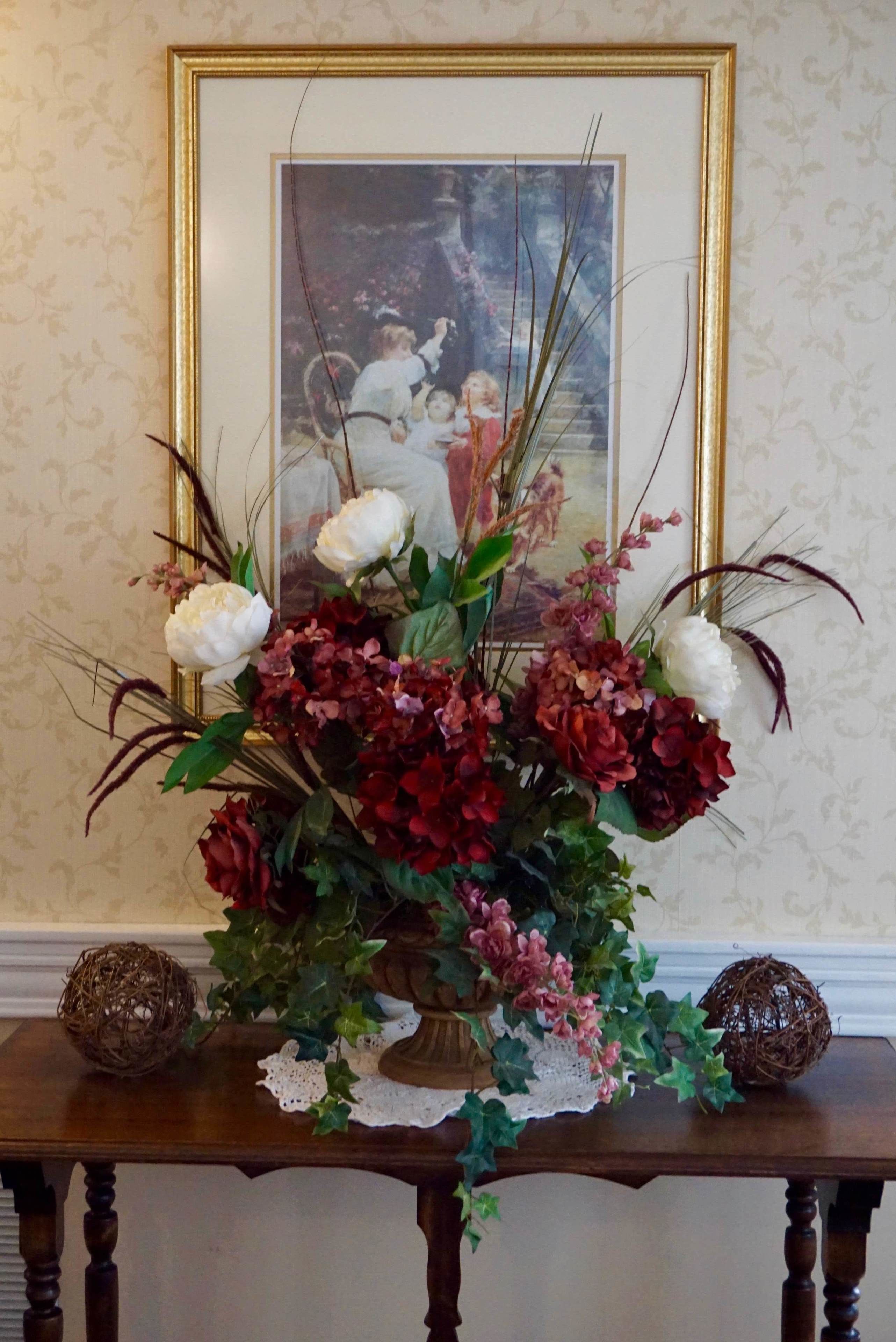 Une table ornée d’un arrangement floral, d’un tableau encadré et de deux sphères décoratives.