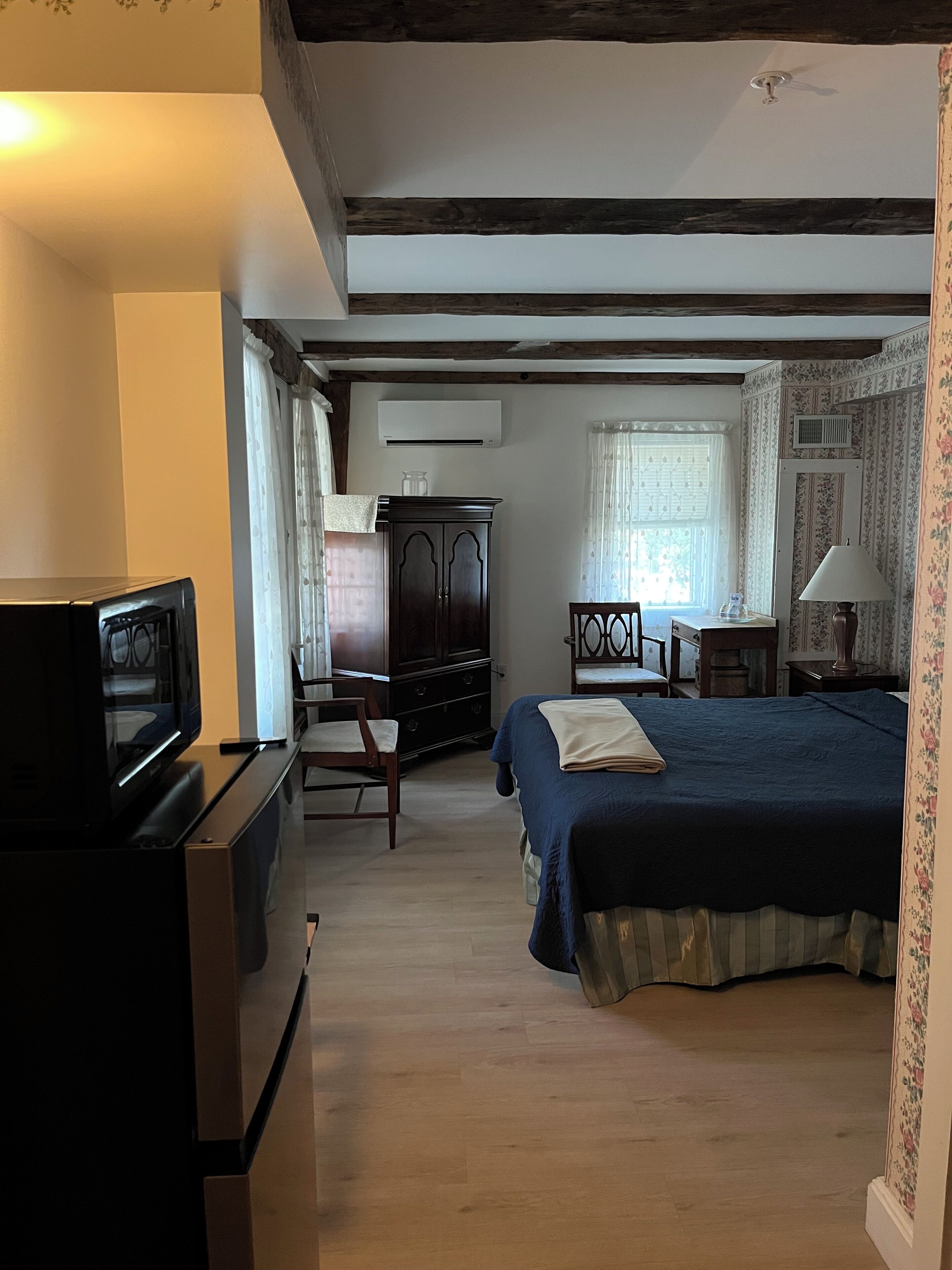 A bedroom with a bed, a desk, a chair, a television, and an air conditioning unit.