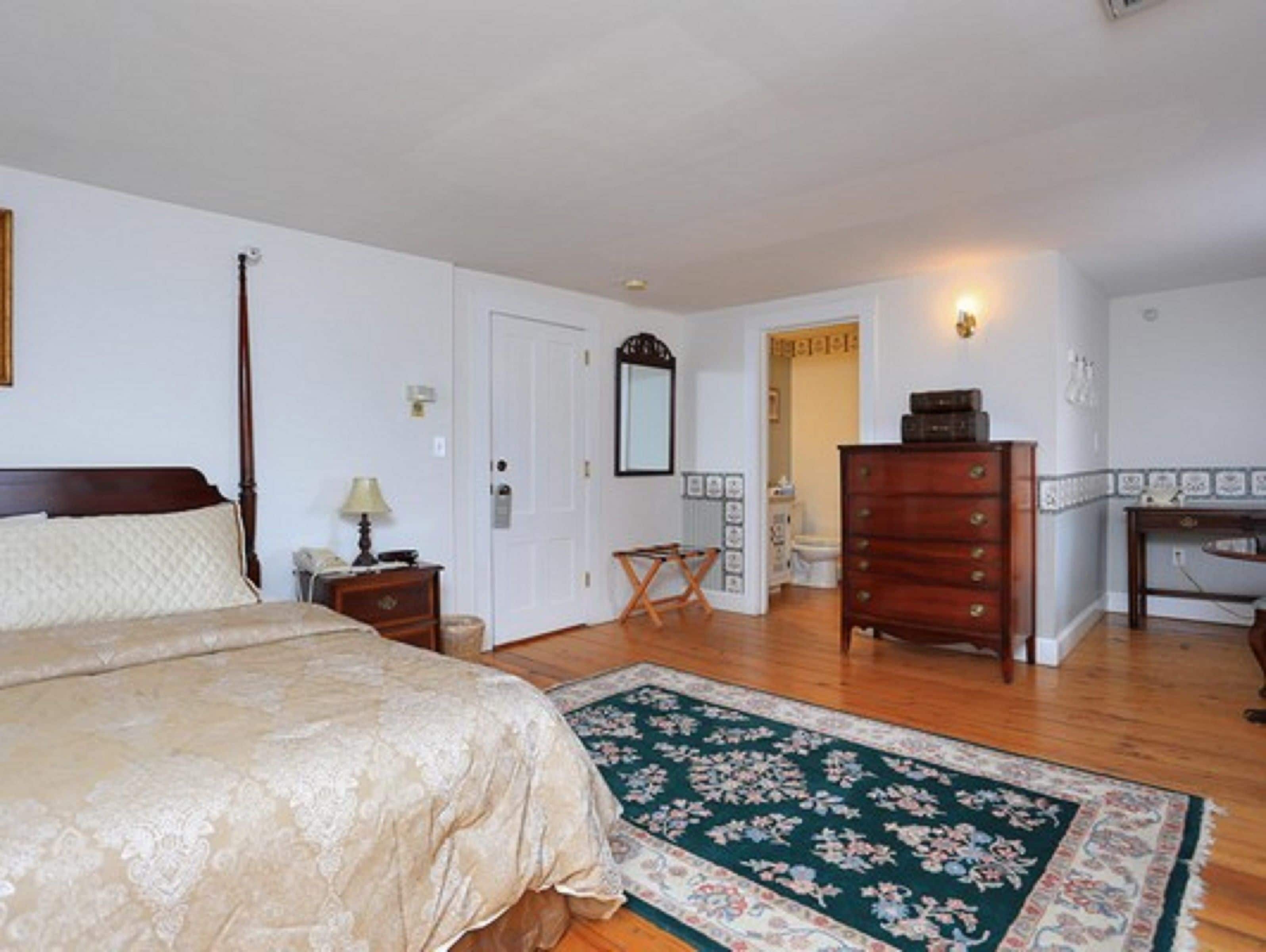 Un dormitorio con una cama grande, un aparador, una mesita de noche, un espejo y una puerta que da a otra habitación.