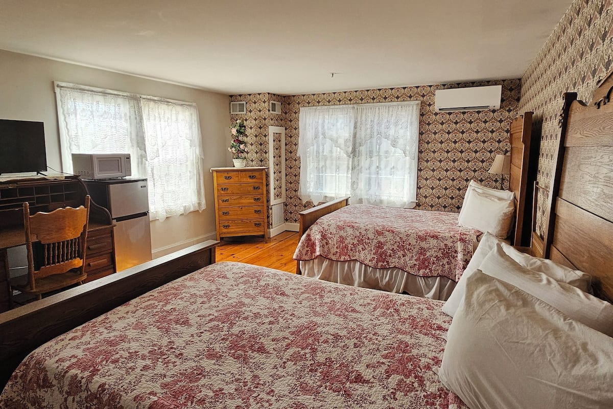 A bedroom with two beds, a desk with a computer, a dresser, and a TV.