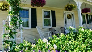 Una casa con porche, barandas blancas y cestas de flores colgantes.