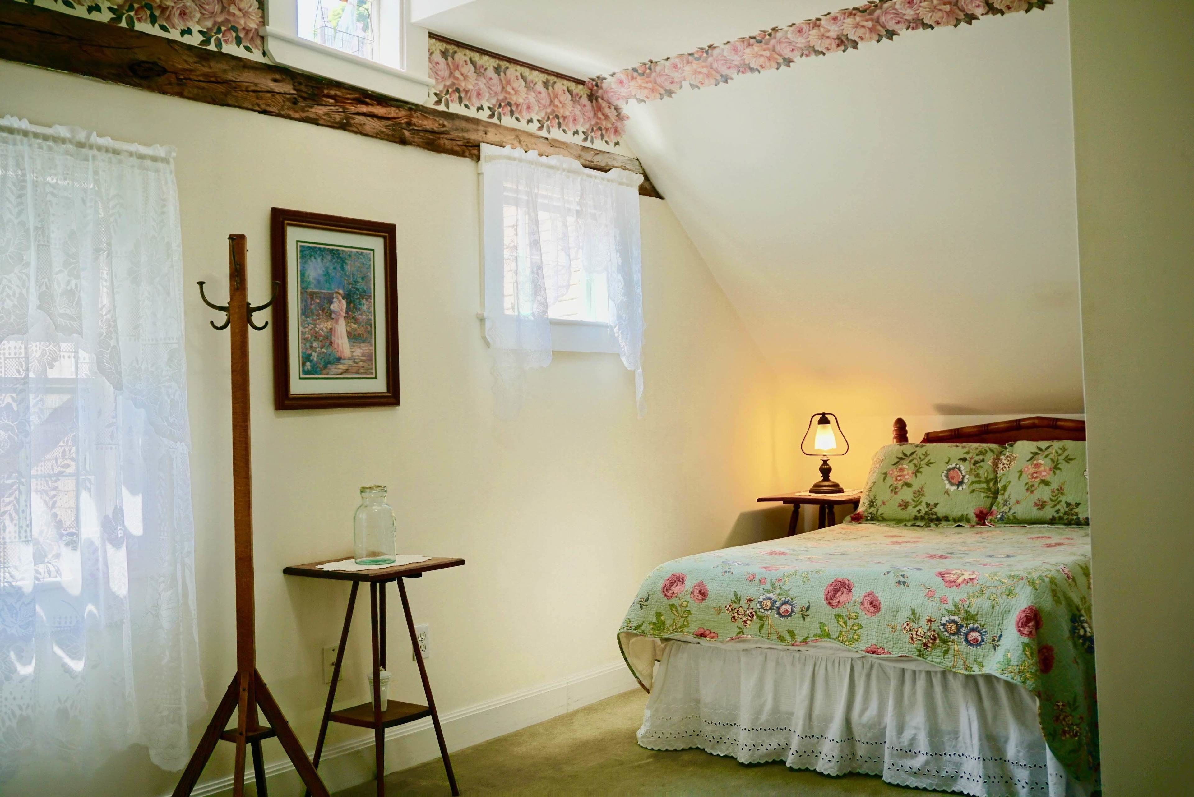 A bedroom with a bed, a nightstand, a lamp, a picture frame, and a window with lace curtains.
