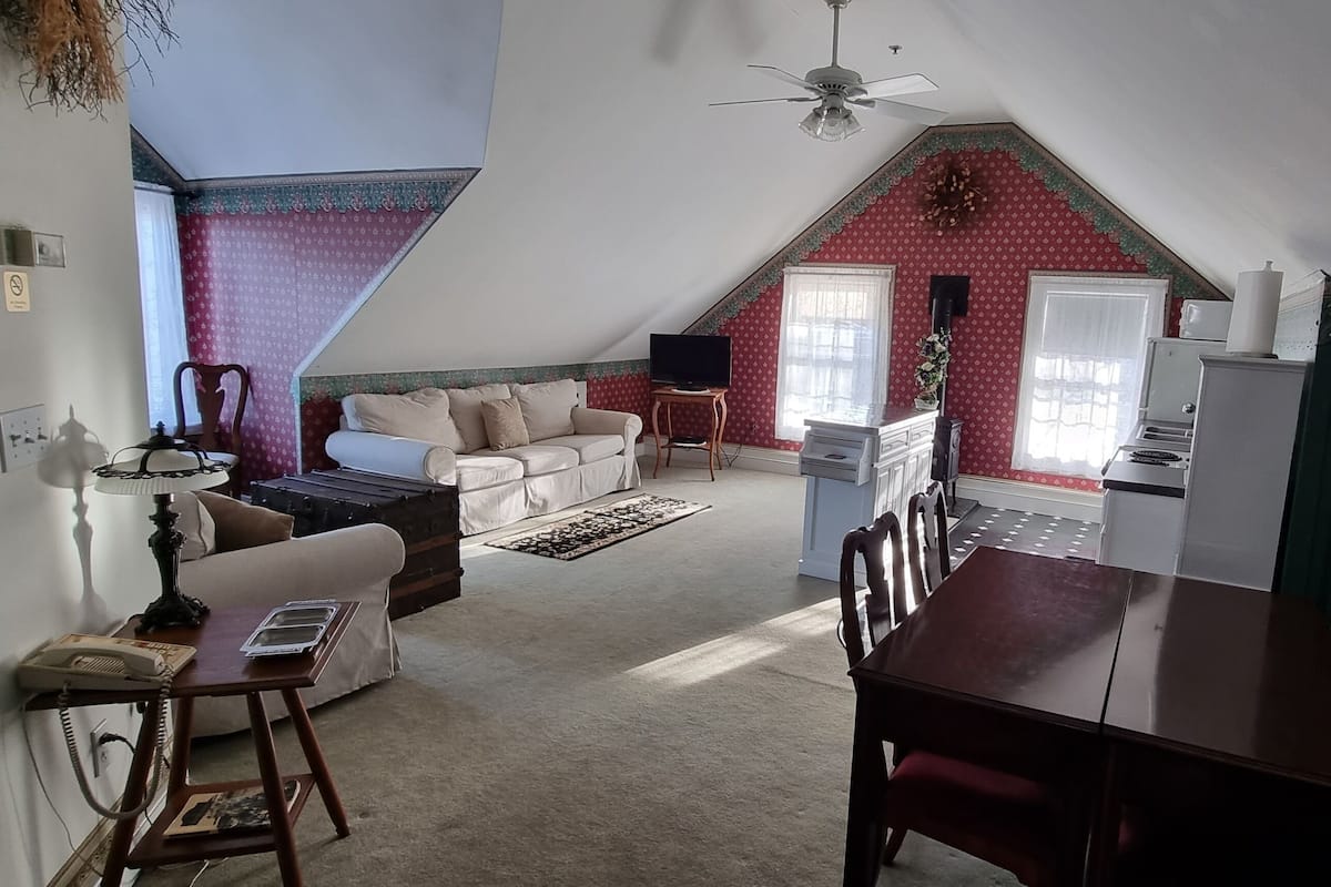 A cozy attic bedroom with a sloped ceiling, a dining table, a sofa, and a TV.