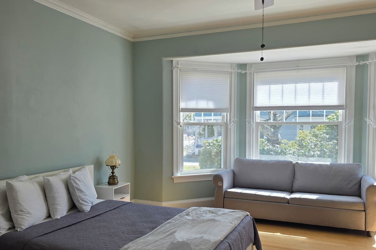 A bedroom with a bed, a nightstand, a lamp, a ceiling fan, and a window with blinds.